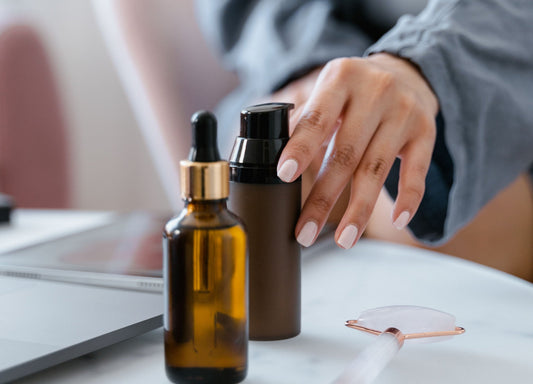 Woman reaching for skincare products with facial oil dropper bottle on vanity